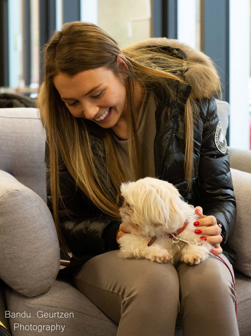 A student sat on a sofa with a white dog in their lap