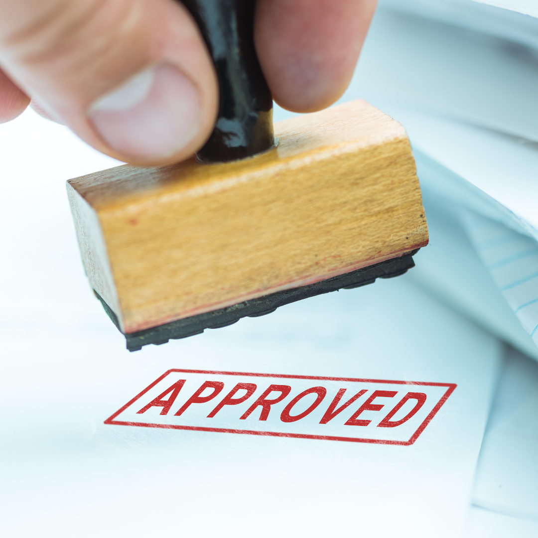 A stamp that has just stamped the word APPROVED in red ink on white paper