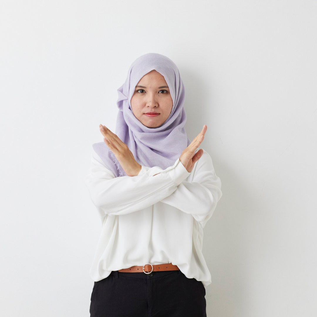 A person wearing a lilac hijab  and white shirt with their arms crossed in a gesture that indicates no