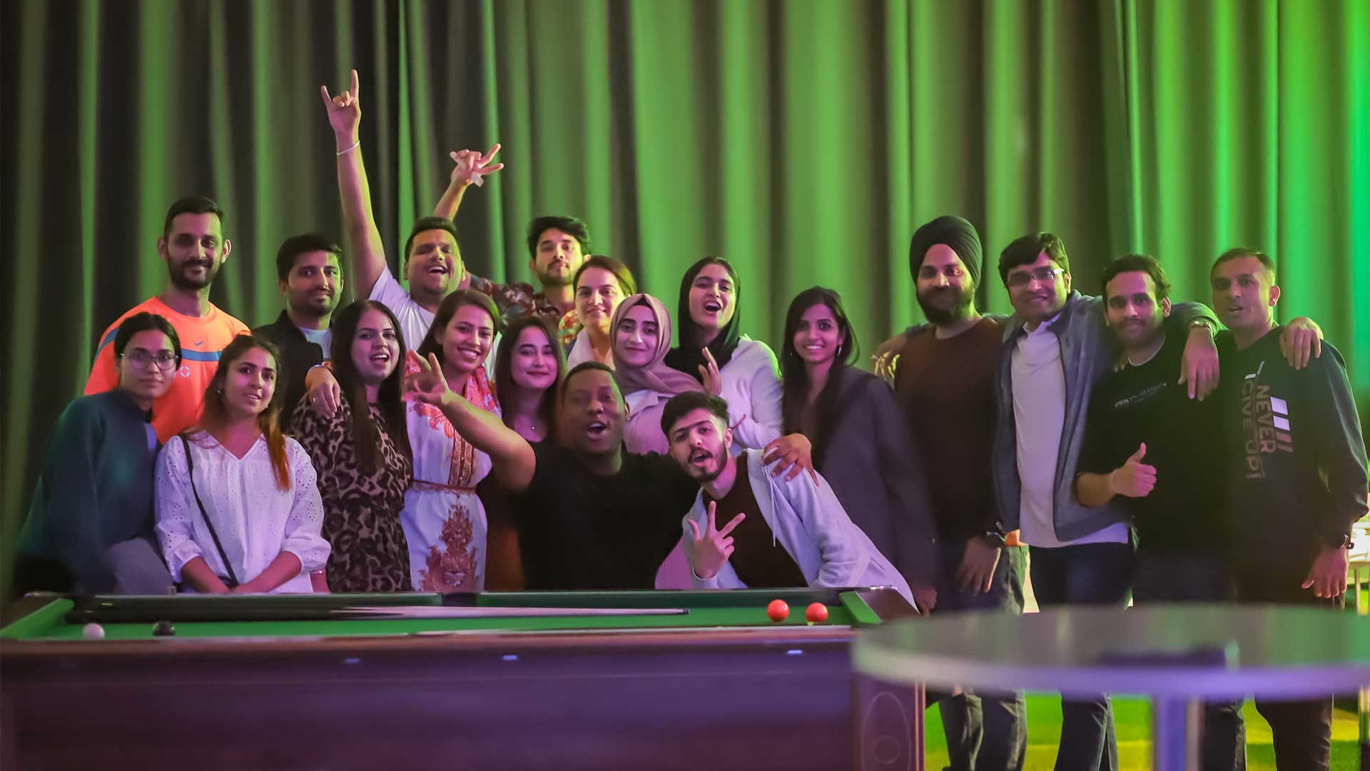 A group of students all posing for the camera by a pool table