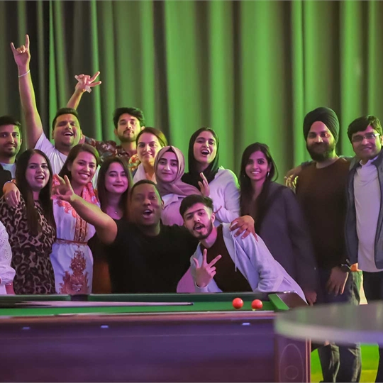 A group of students all posing for the camera by a pool table
